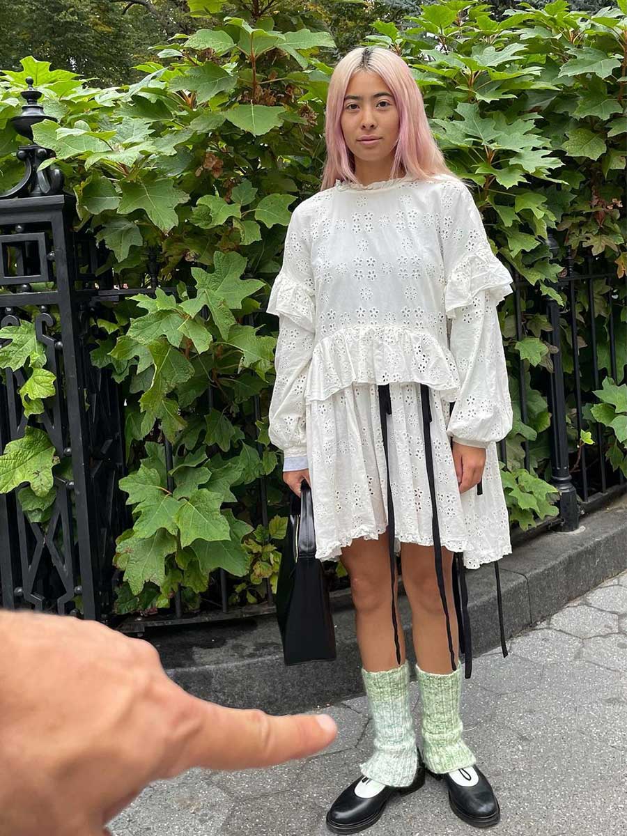 Girl wearing white frilly long sleeve knee length white lace dress with black ribbon wrapped with green leg warmers, black loafers, and white socks by Michelle Li on Instagram