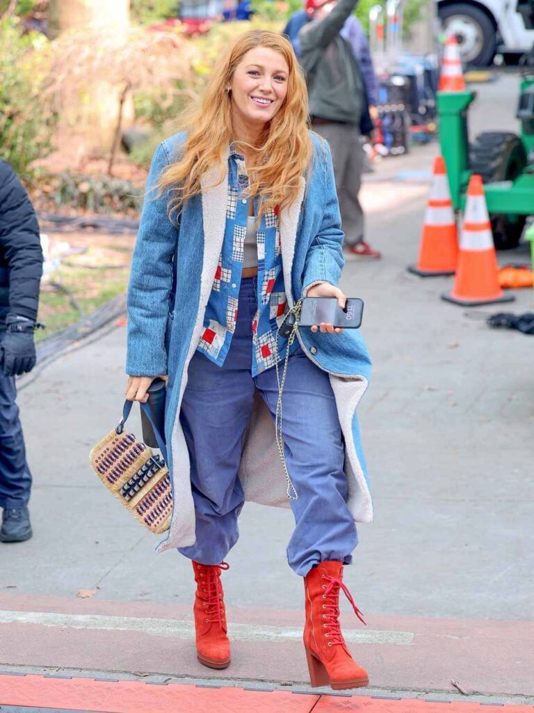 Blake Lively wearing double denim–a long denim jacket over a patchwork jacket with blue denim pants and tall red platform heeled boots as Lily Bloom in movie adaptation of Colleen Hoover's book "It Ends with Us"