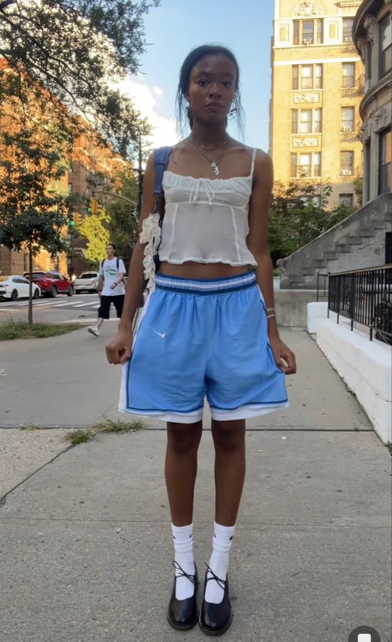 Young African American Gen-Z woman wearing a sheer camisole tank top with blue basketball shorts, tall socks and mary jane ballet flats