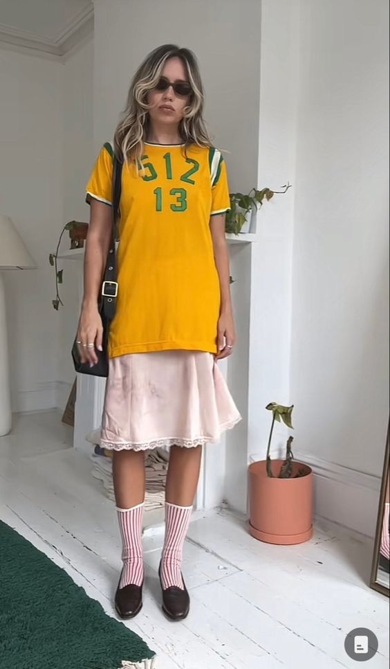 Young Gen-Z woman wearing an eclectic, thrifted outfit: soccer jersey, slip dress, tall socks and flats